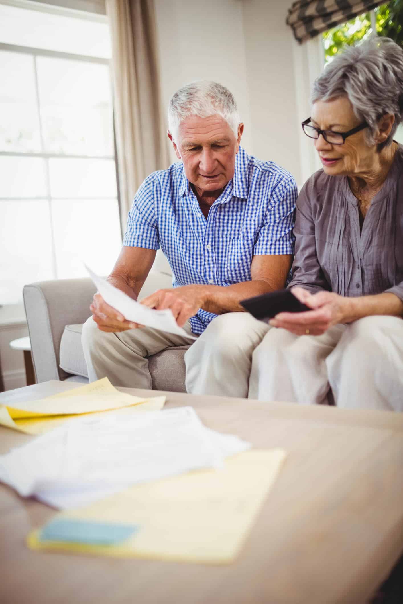 Senior man and woman look at documents together on the couch in their living room