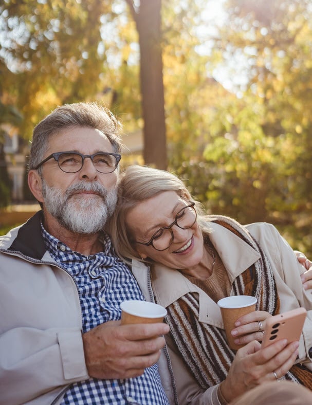 Happy older couple sitting outside having coffee and listening to the radio on a phone